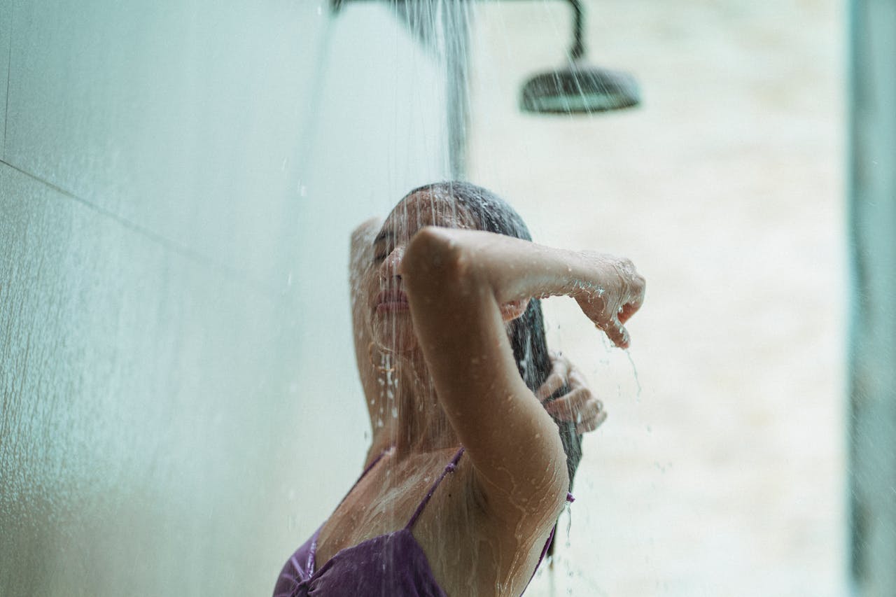 A young woman in a swimsuit enjoys an outdoor shower, capturing a moment of relaxation and tranquility.